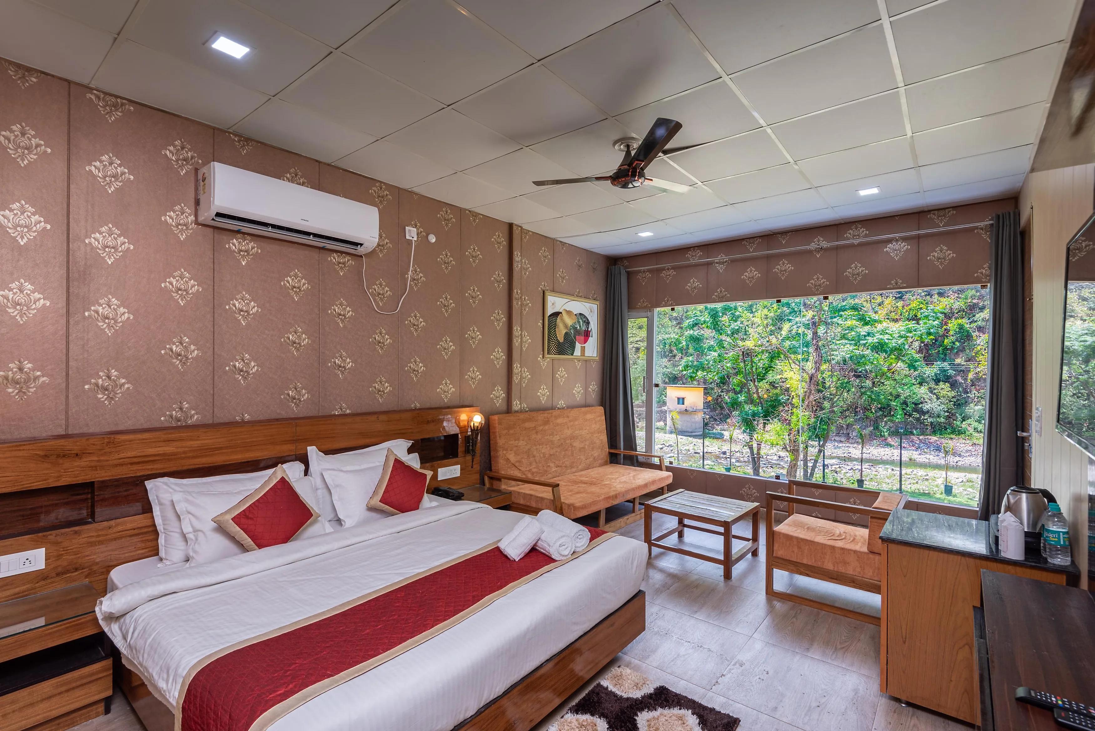 a bedroom with a large bed and window view and chairs at sukham raasa river in rishikesh hotel_Image